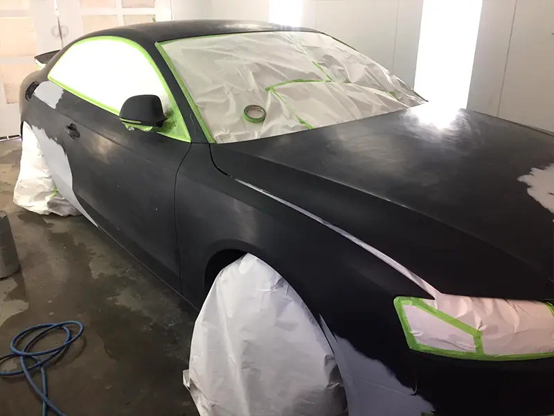 Black Audi with minor surface dents and scratched paint before professional refinishing